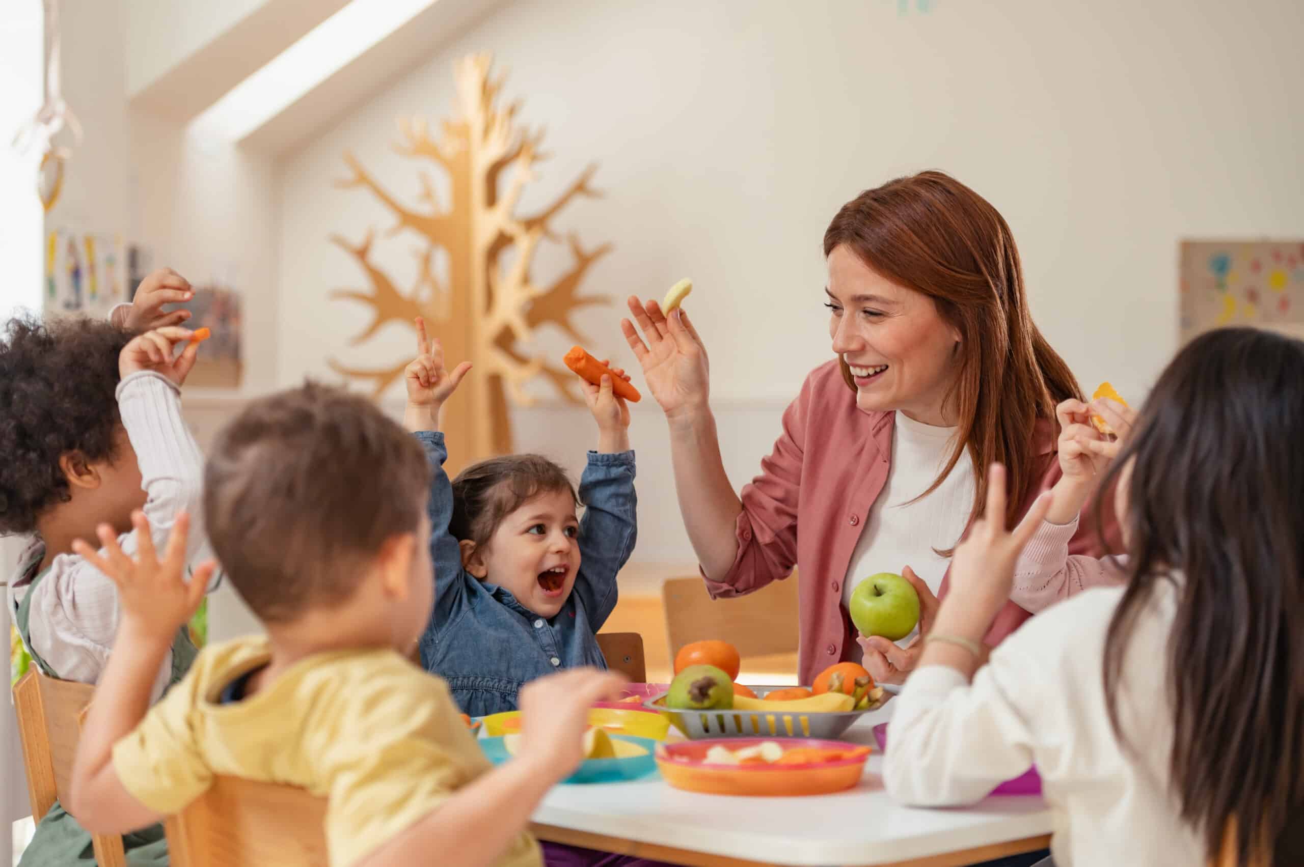 Teacher and joyful children enjoy a playful snack time with fruits and vegetables around a table.