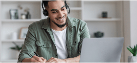 Smiling person wearing headphones, writing notes in front of a laptop.