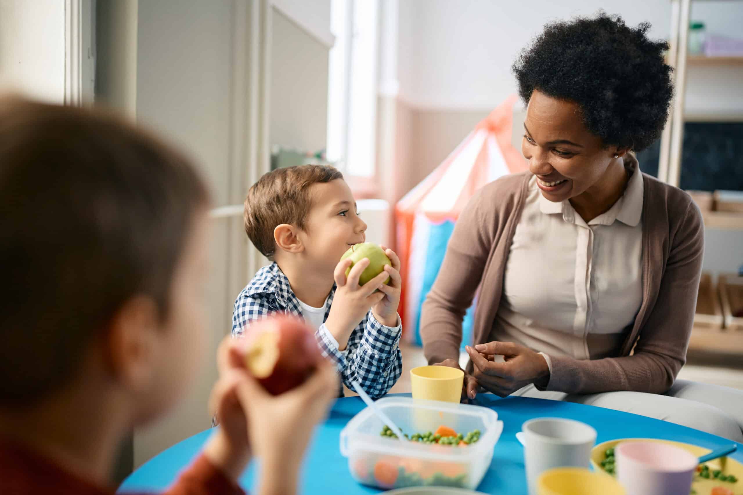 Child holding an apple, smiling at an adult at a table with healthy food.
